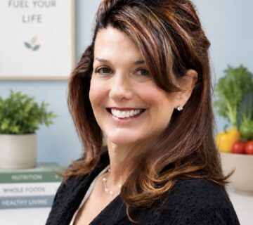 Shannon Rene, RDN, LDN, CFMP, founder of Fit N Pilates and Fit N Vitality in Plano, TX, smiling in her office surrounded by nutrition books and fresh vegetables